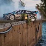 Ford Performance: Ken Block's Ultimate Exotic Playground in Dubai Gymkhana 2 Ken Block Rally car in drift over water with smoke, excitement and a spectacular sunset view.